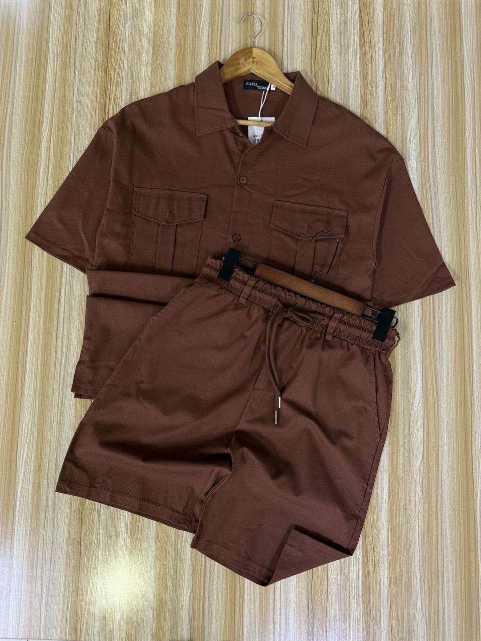 Brown shirt and shorts set on a hanger against a striped wall.