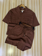 Brown shirt and shorts set on a hanger against a striped wall.