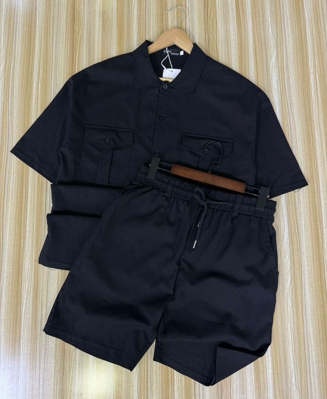 Black shirt and shorts set on a hanger against a striped background