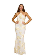 Woman wearing a white and gold evening gown in front of beige curtains