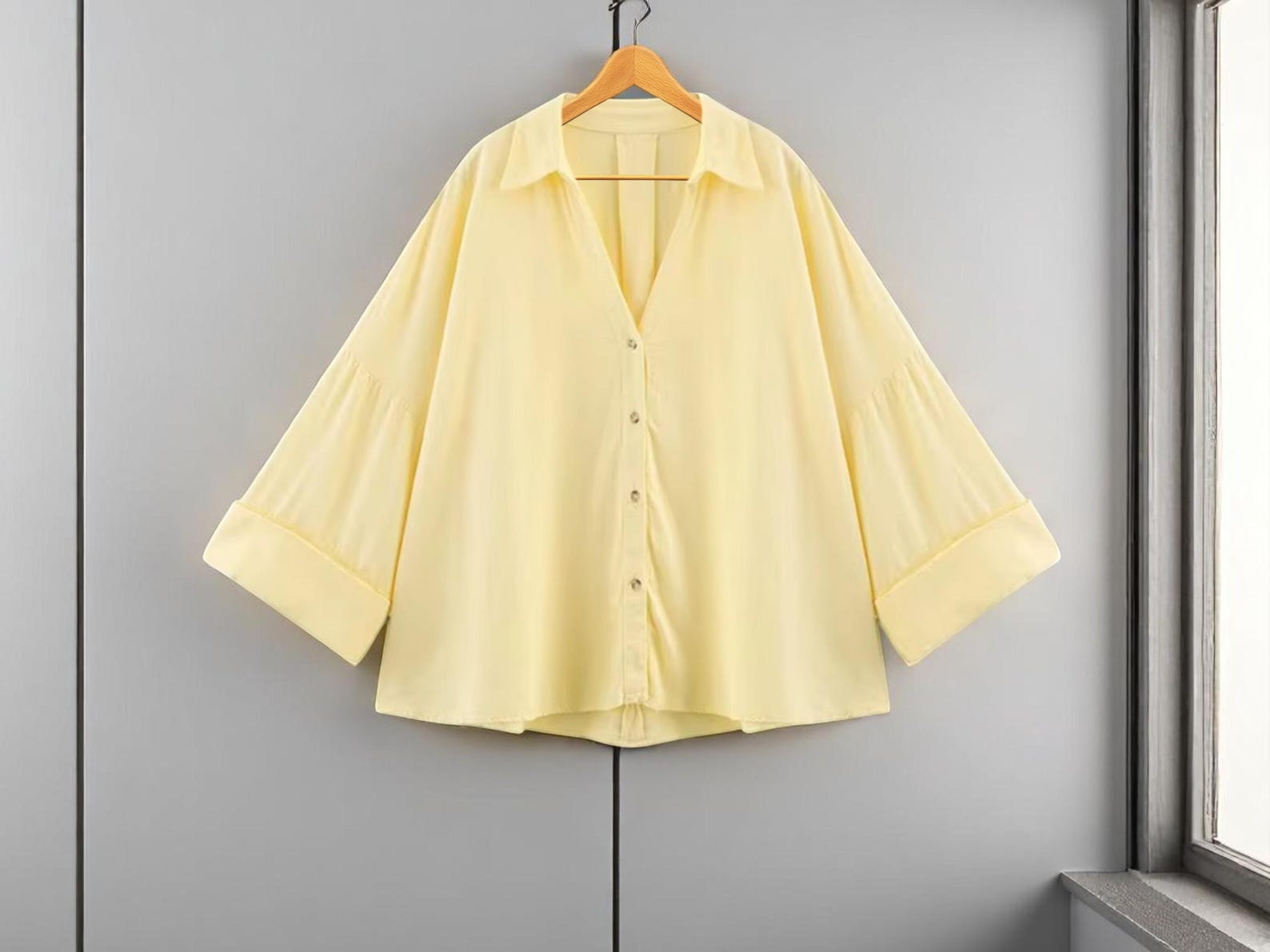 Yellow shirt on a hanger against a gray wall with a window.