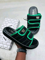 Black sandals with green straps on a light gray surface