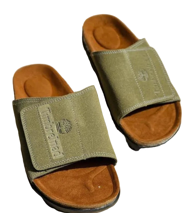 Pair of green slides with brown soles on a beige background