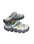 White clogs with colorful designs held against a green leafy background