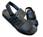 Black sandal with straps held by a hand on a gray surface